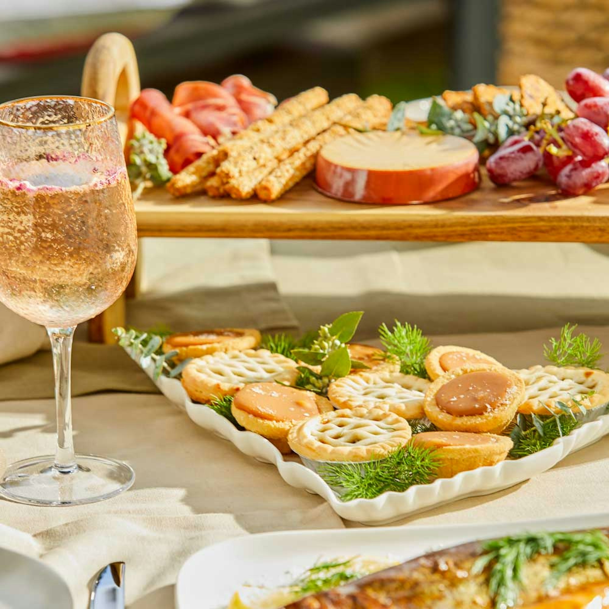 Your Ultimate Guide To Secret Santa Gift Ideas. Christmas tree serving platter with mince pies and caramel tarts next to a cheese platter and wine.