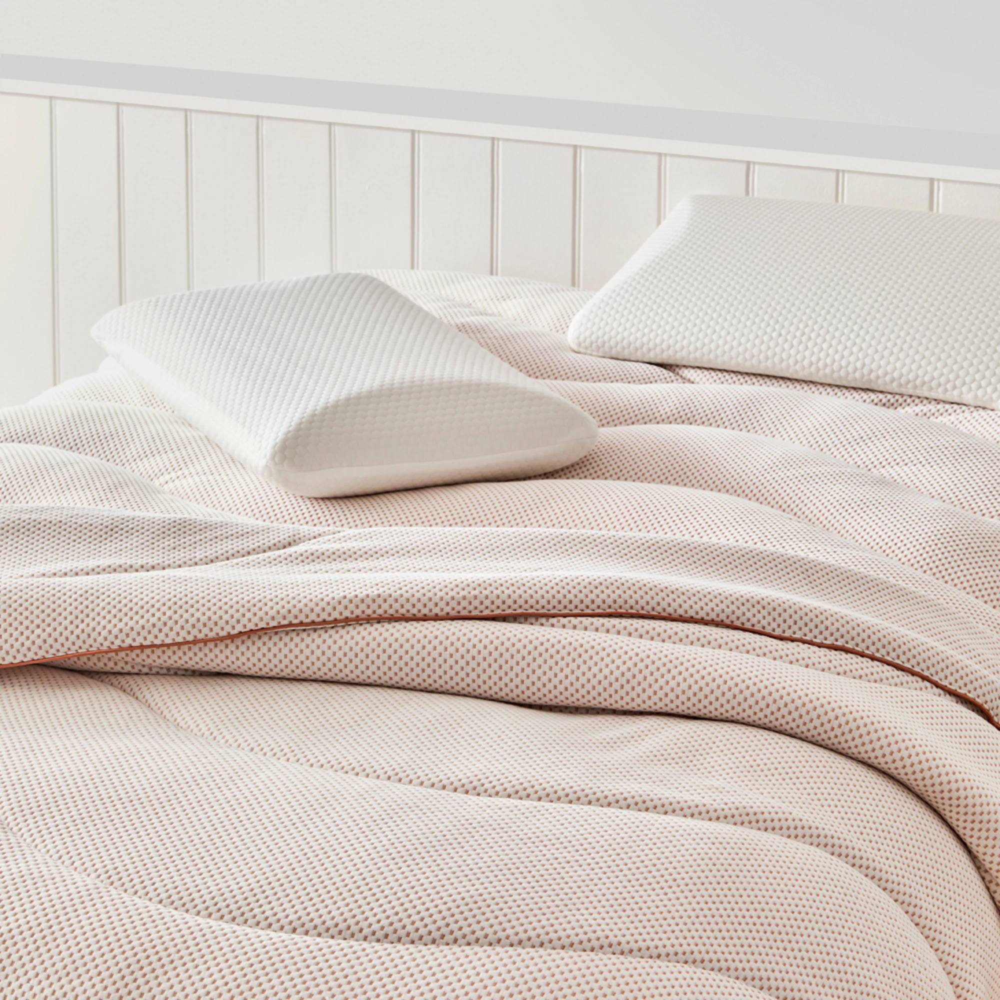 Deborah Hutton Pure Balance Copper Quilt in soft blush tones with a textured jacquard finish, styled on a bed with matching white pillows