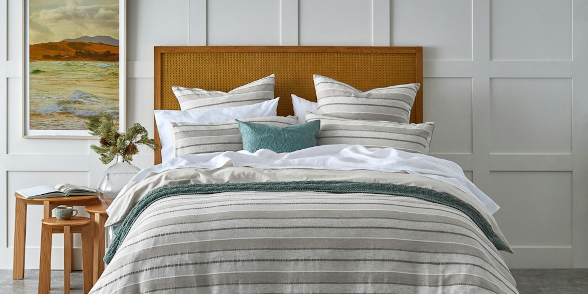 Striped bedroom setting in cool tones with layered cushions, side tables and throws.