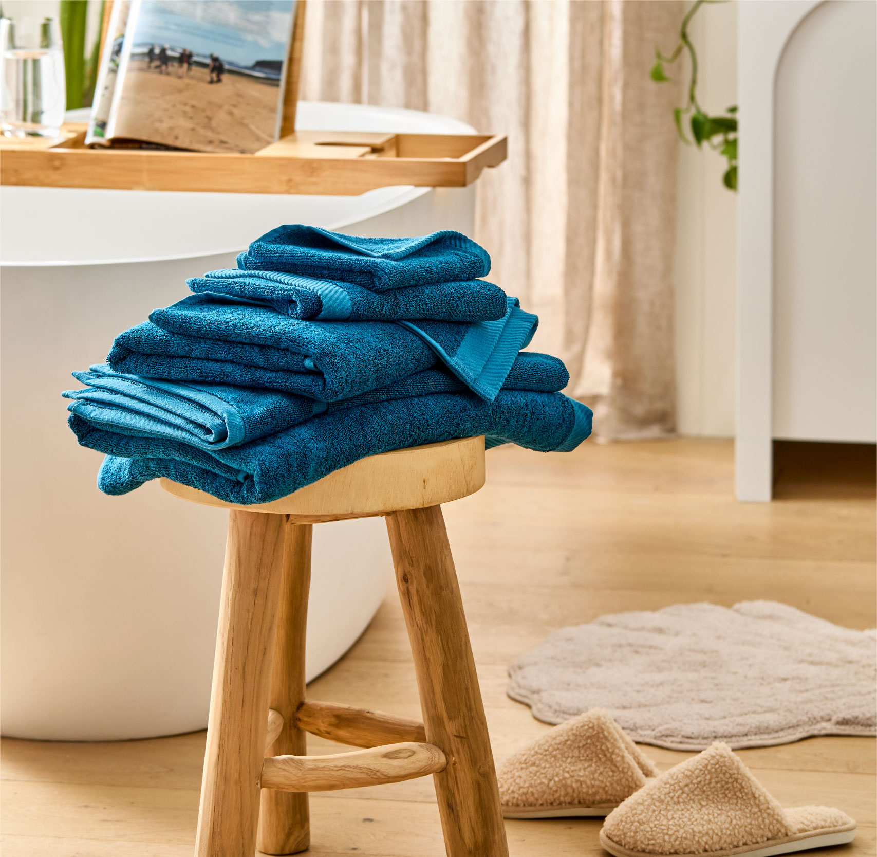 Blue Bath Towels on a stool, slippers next to bath mats