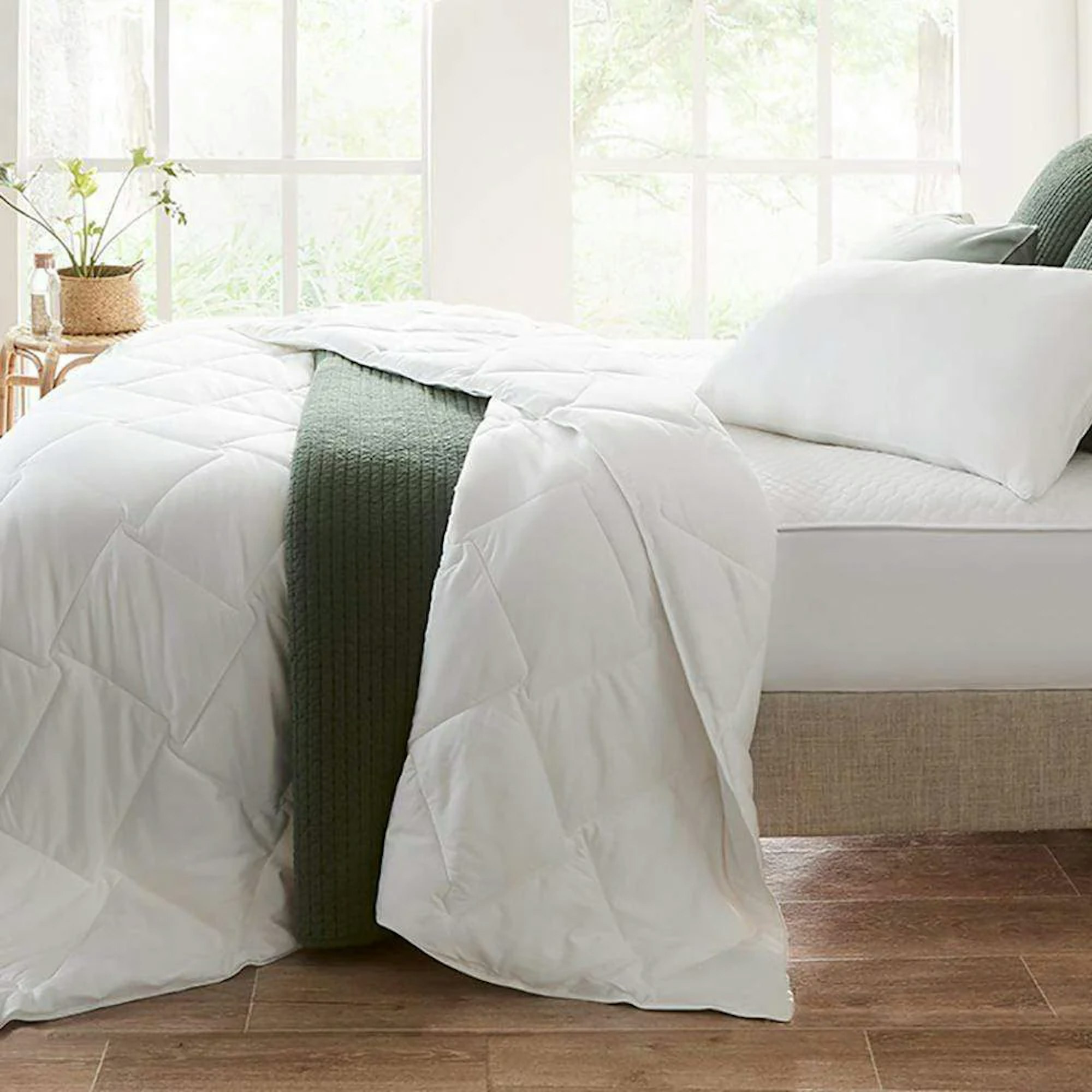 Side profile of a white doona on a bed with white pillows, white fitted sheet, and a dark green throw