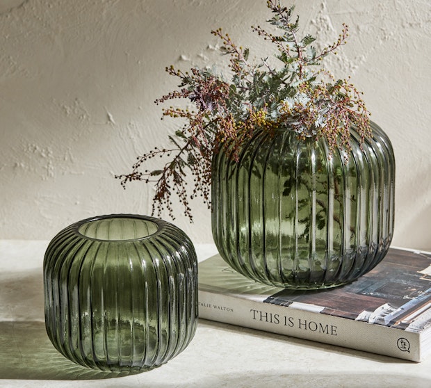 Two green ribbed vases with flowers sitting on books