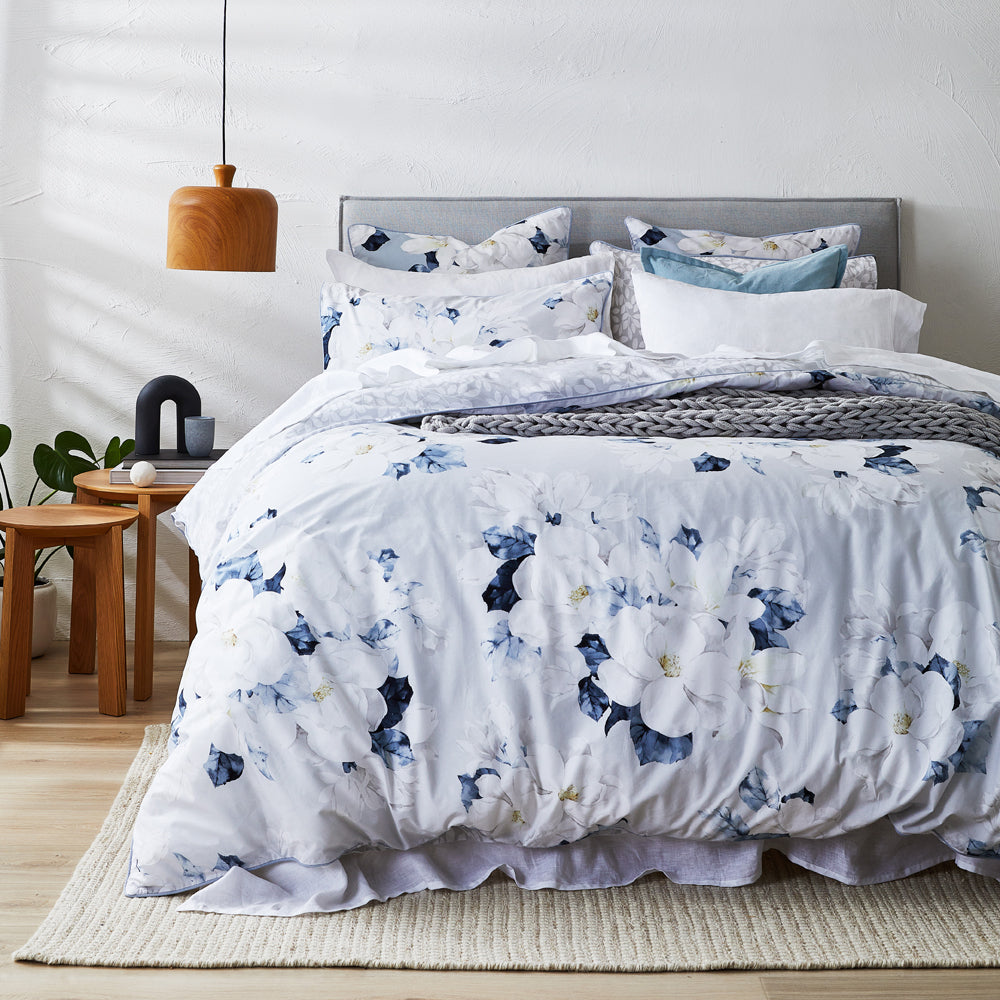 A quilt cover set with magnolia flower design in white and blue colors, displayed on a bed with matching pillowcases.
