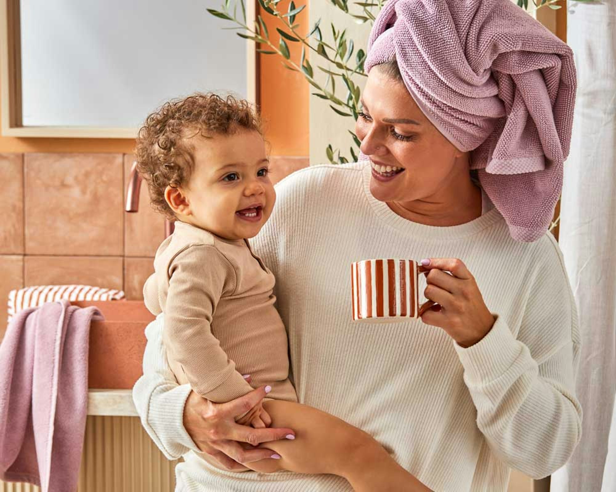 Mother's day gift guide. Mother wearing a towel on their head, holding child and a mug