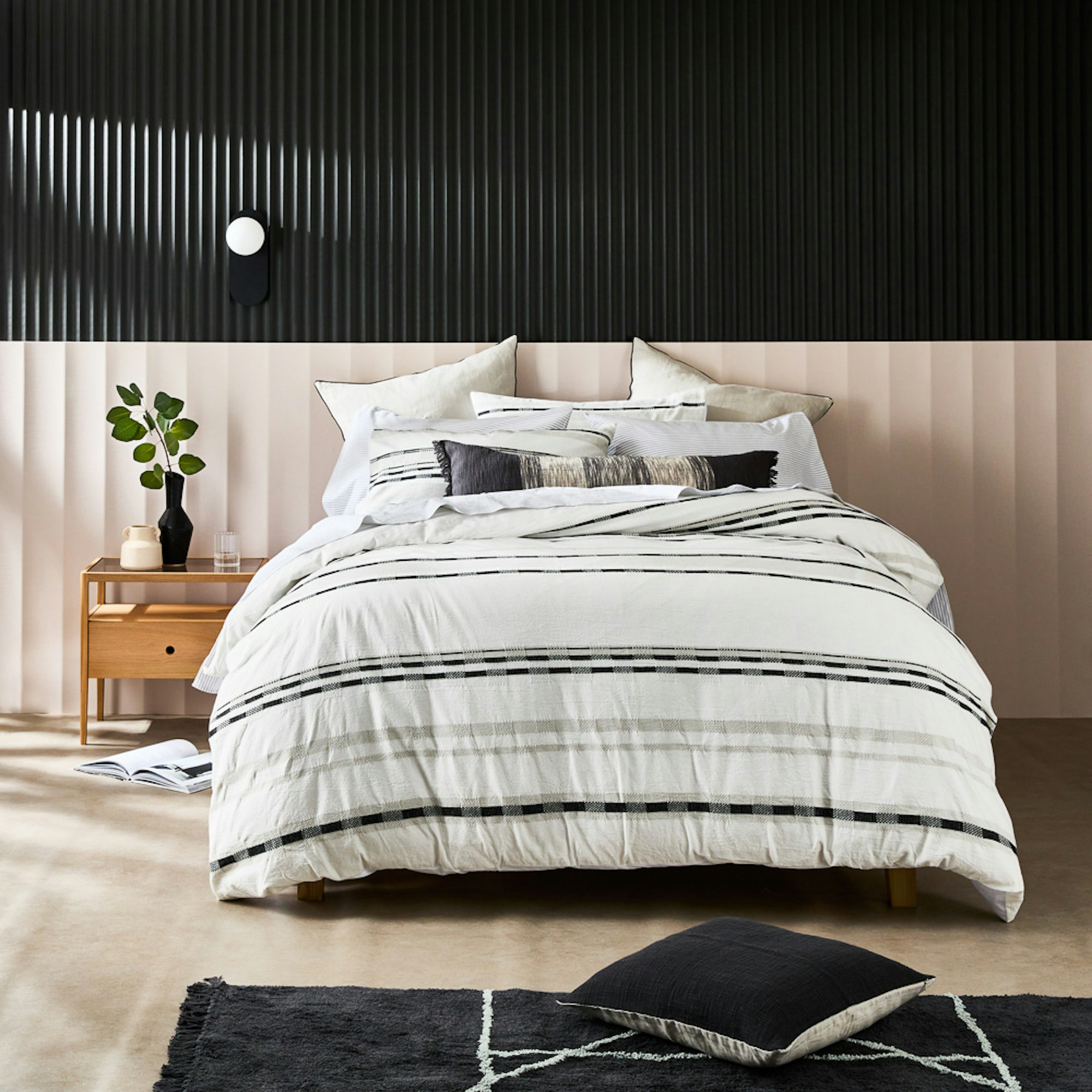 Neale Whitaker SS23 Yamba Quilt Cover set. Bed dressed in white with black and green stripes in a moody monochromatic room.