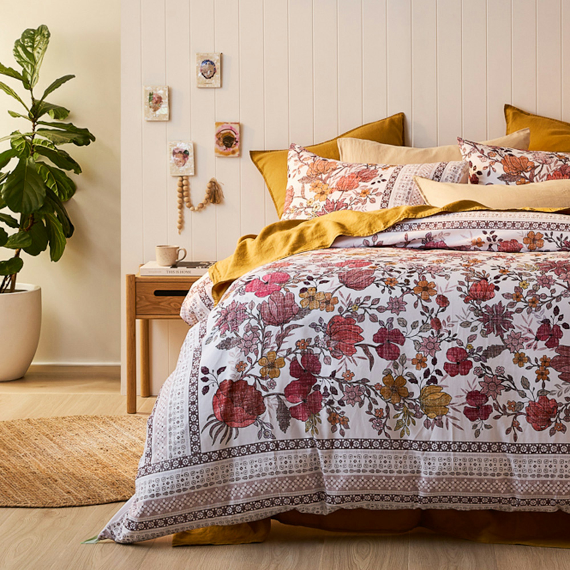 Warm low light complete bedroom setting with layered pillows, bedside table and plant