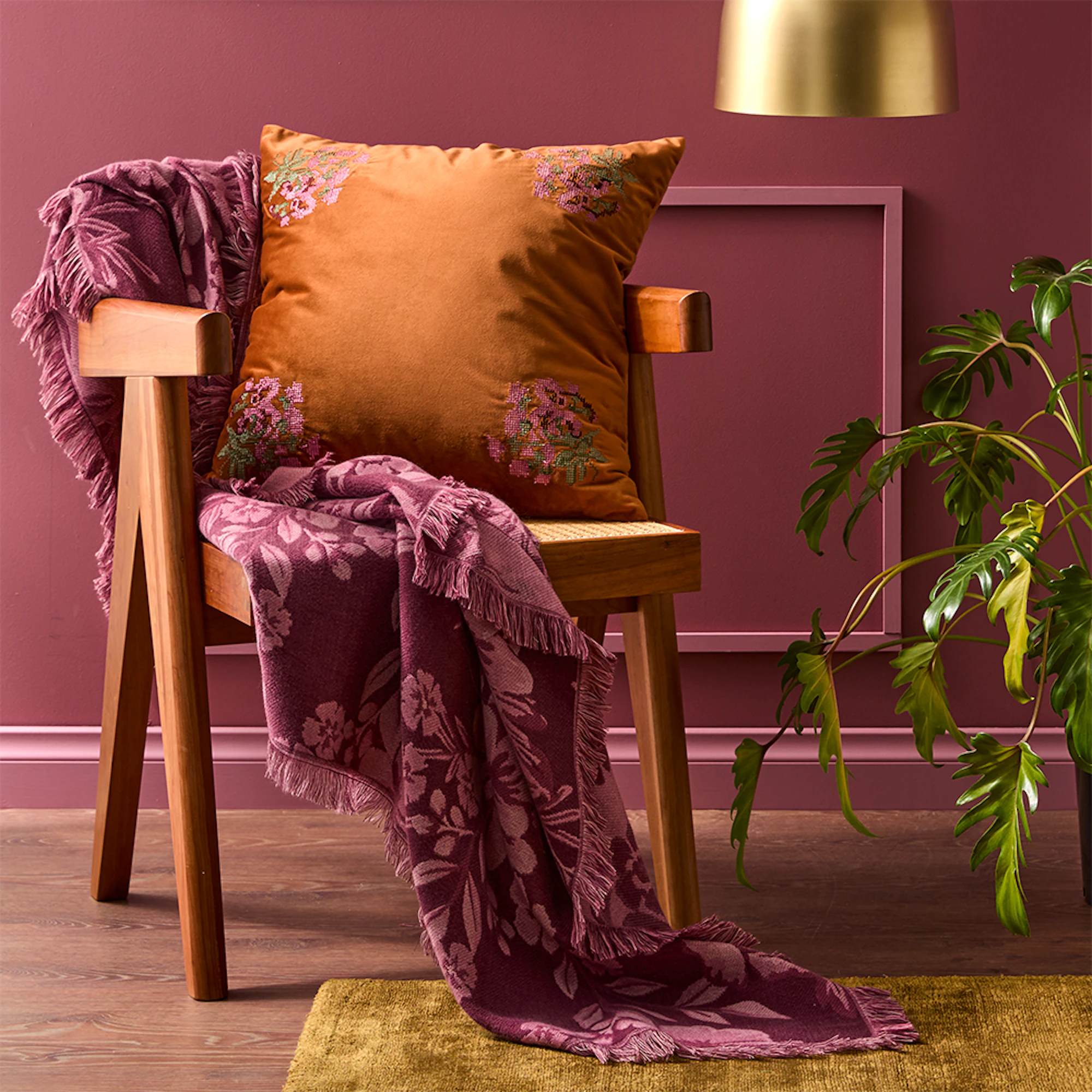 MyHouse Norma Throw draped over a timber armchair, featuring a floral woven pattern in rich plum tones with decorative fringed edges