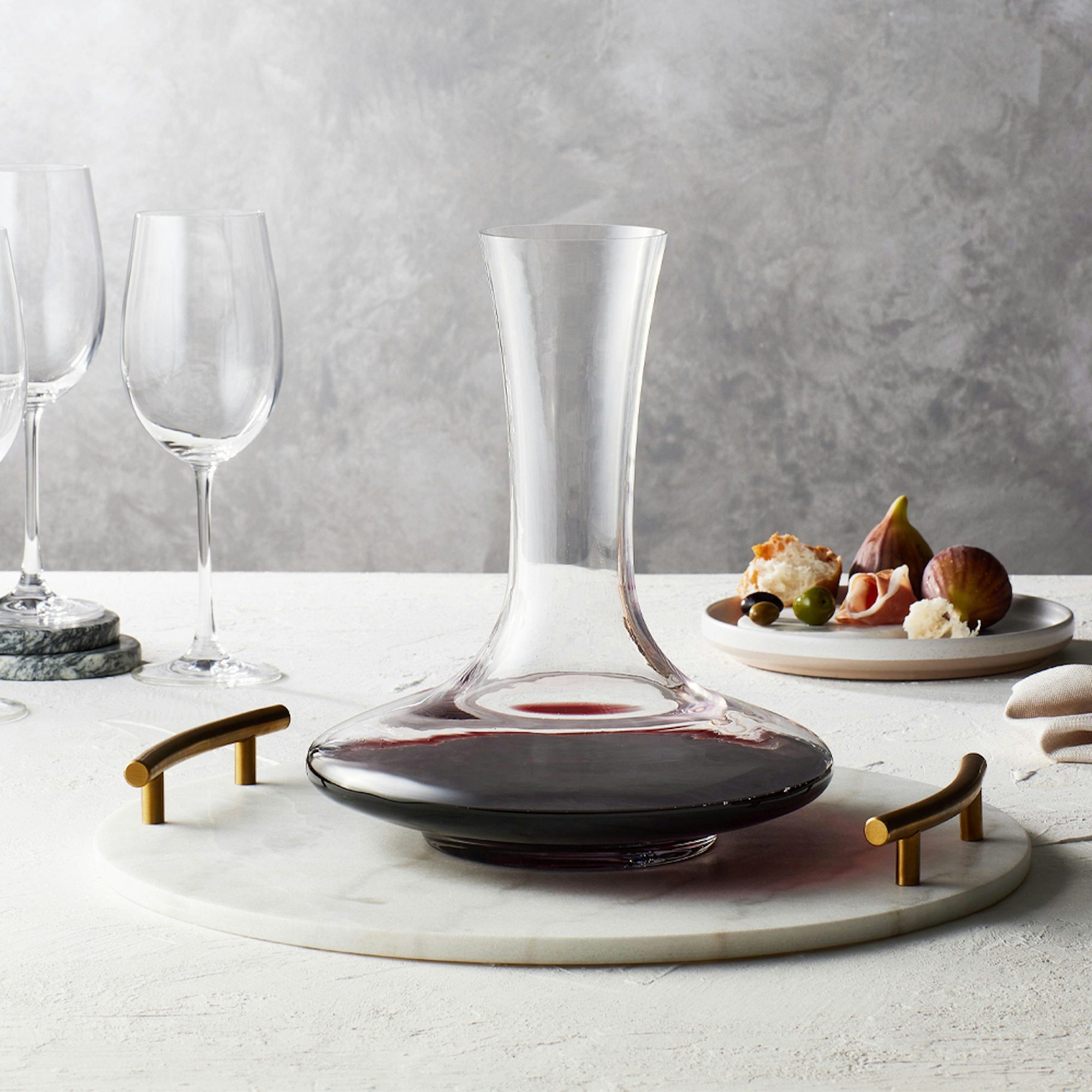 Wine decanter filled with red wine on marble board with glasses and fruit