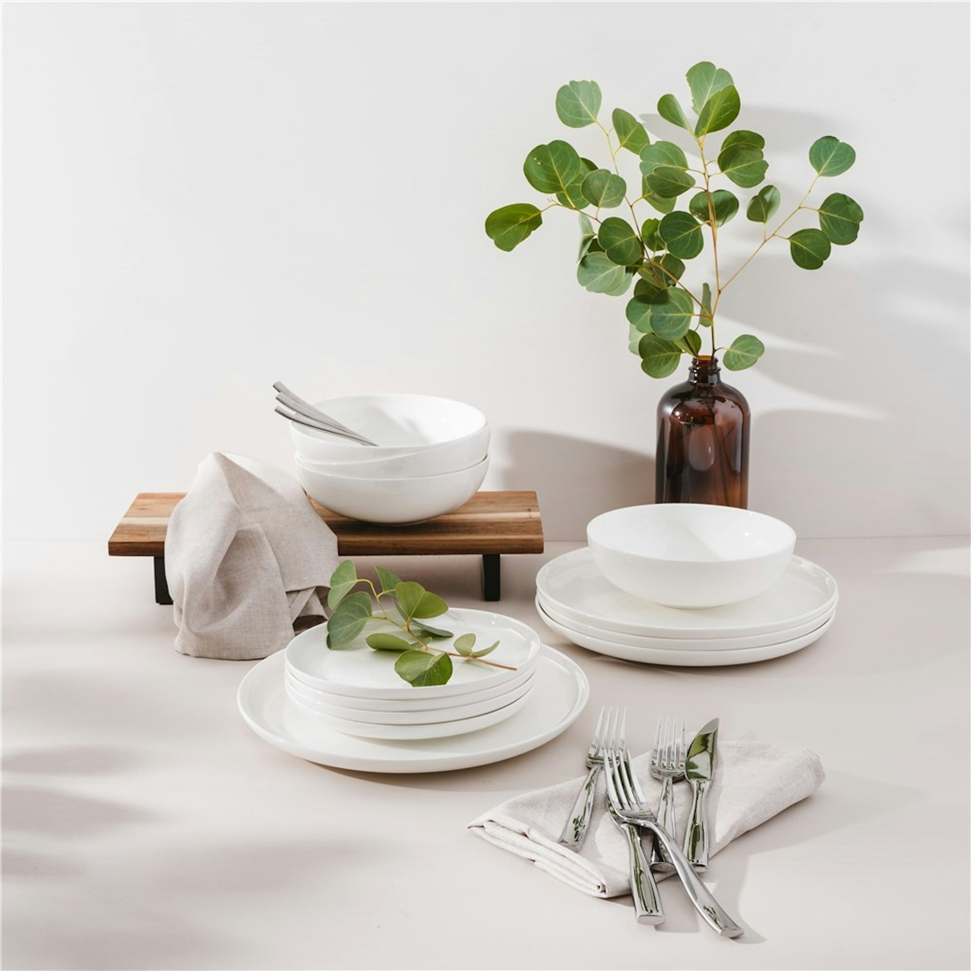 white dinner set stacked with greenery in vase