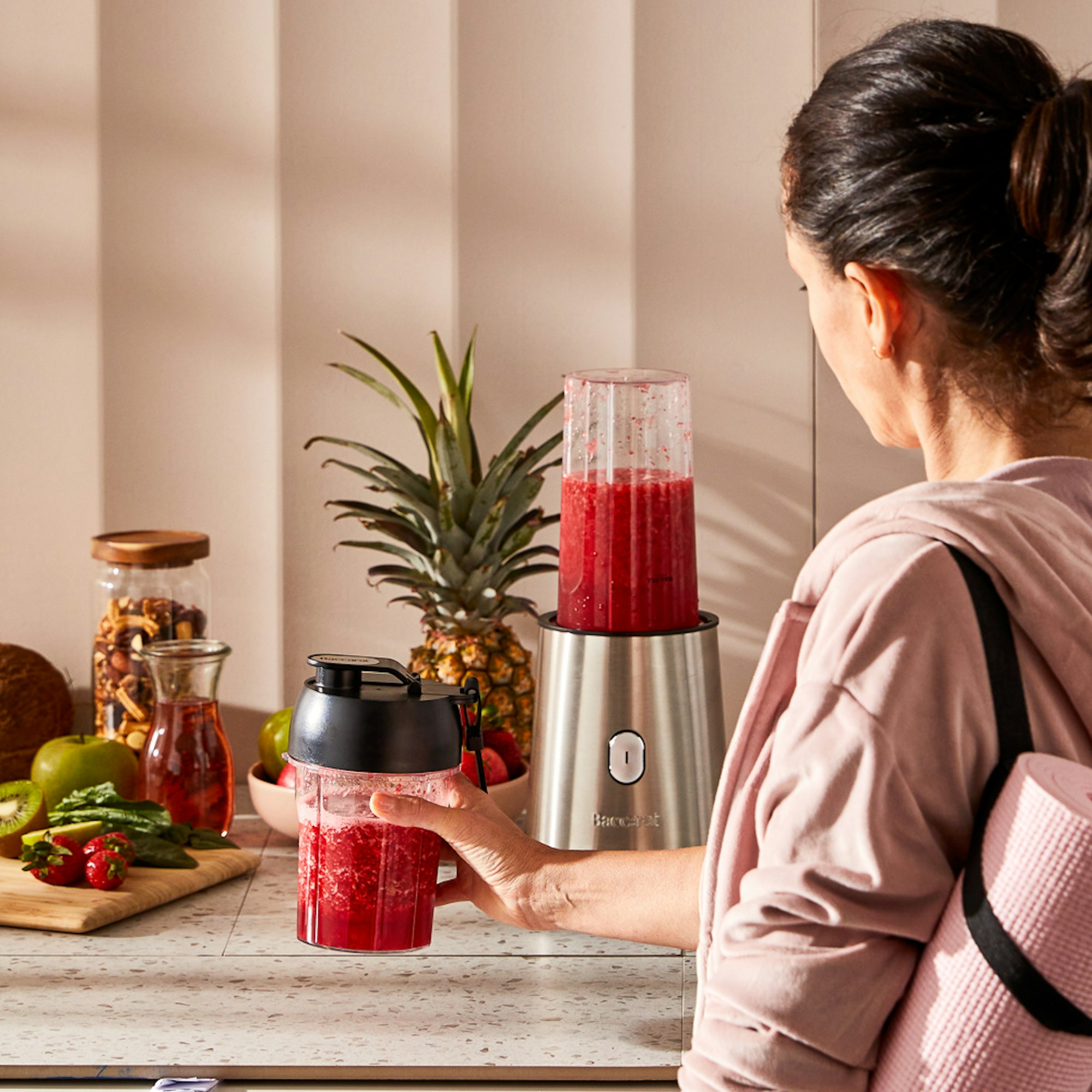 woman in gym clothes picking up berry smoothie by the blender