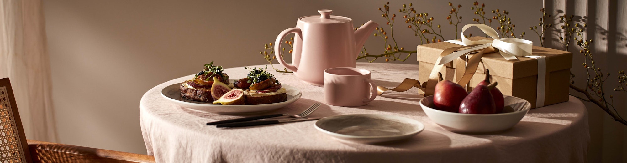 table setting with pink tablecloth, pink teapot and cup, brunch and present