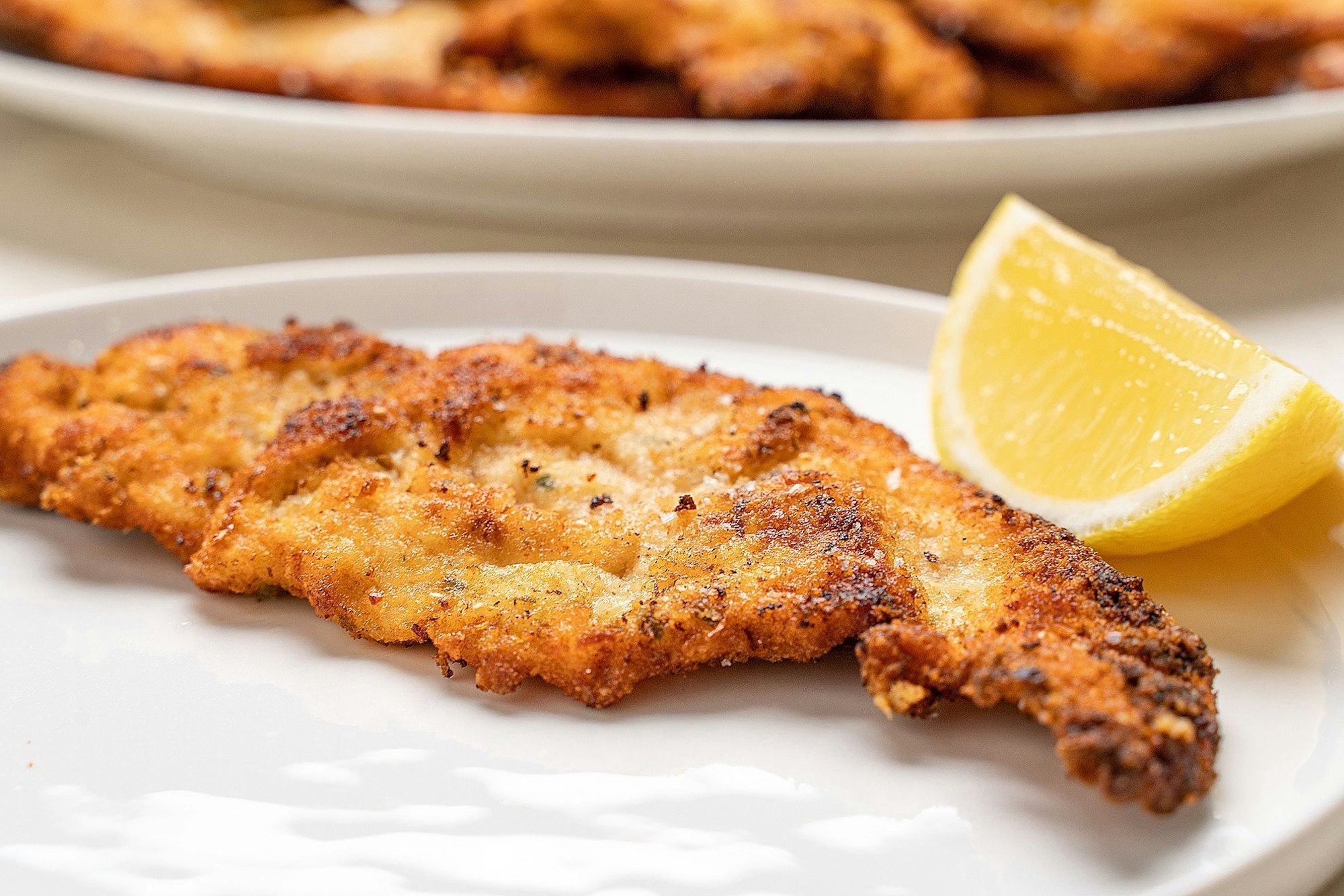 austrian chicken schnitzel on plate besides a lemon wedge