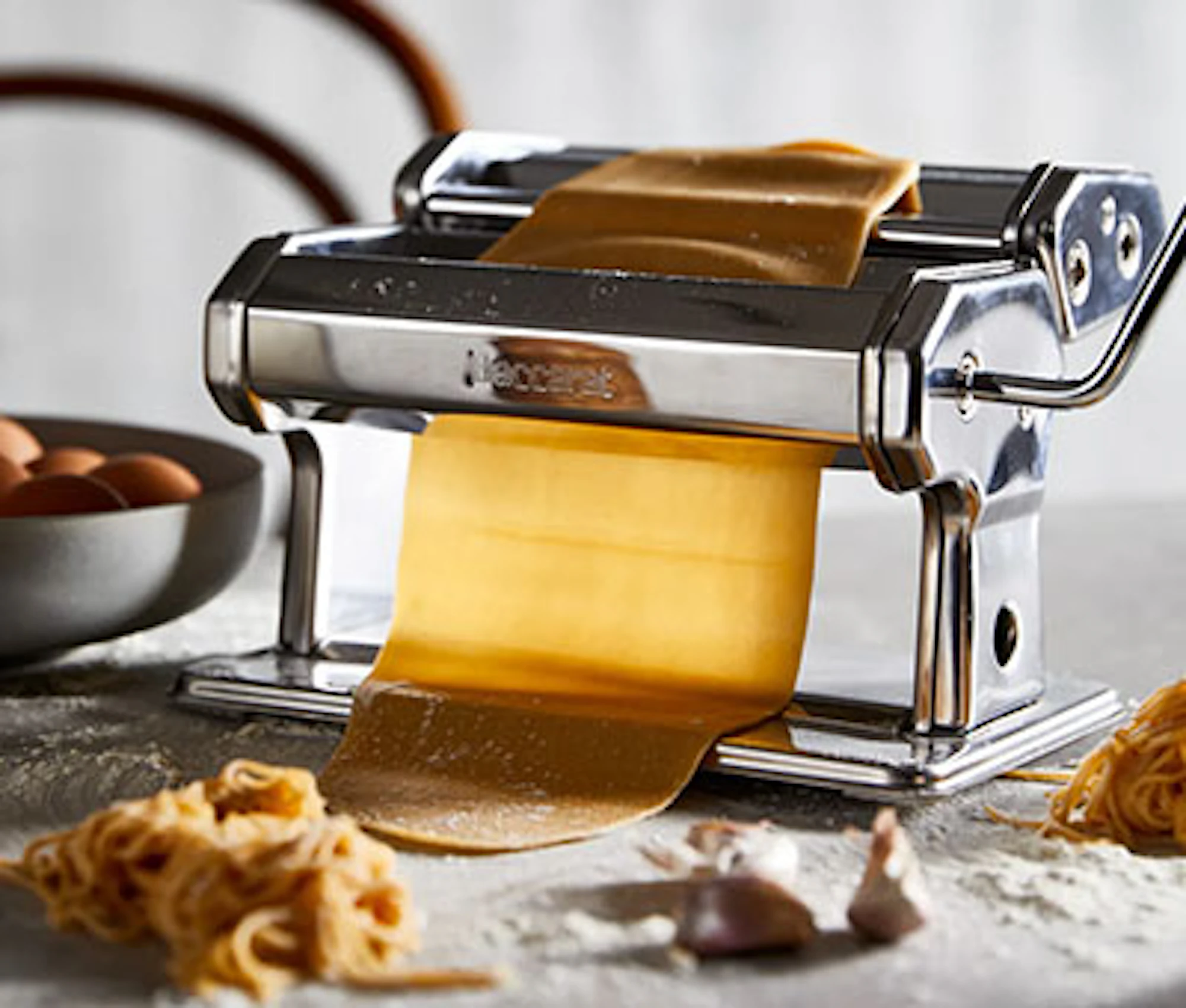 Robins Kitchen rolling fresh pasta dough on a floured countertop beside homemade pasta and baking ingredients