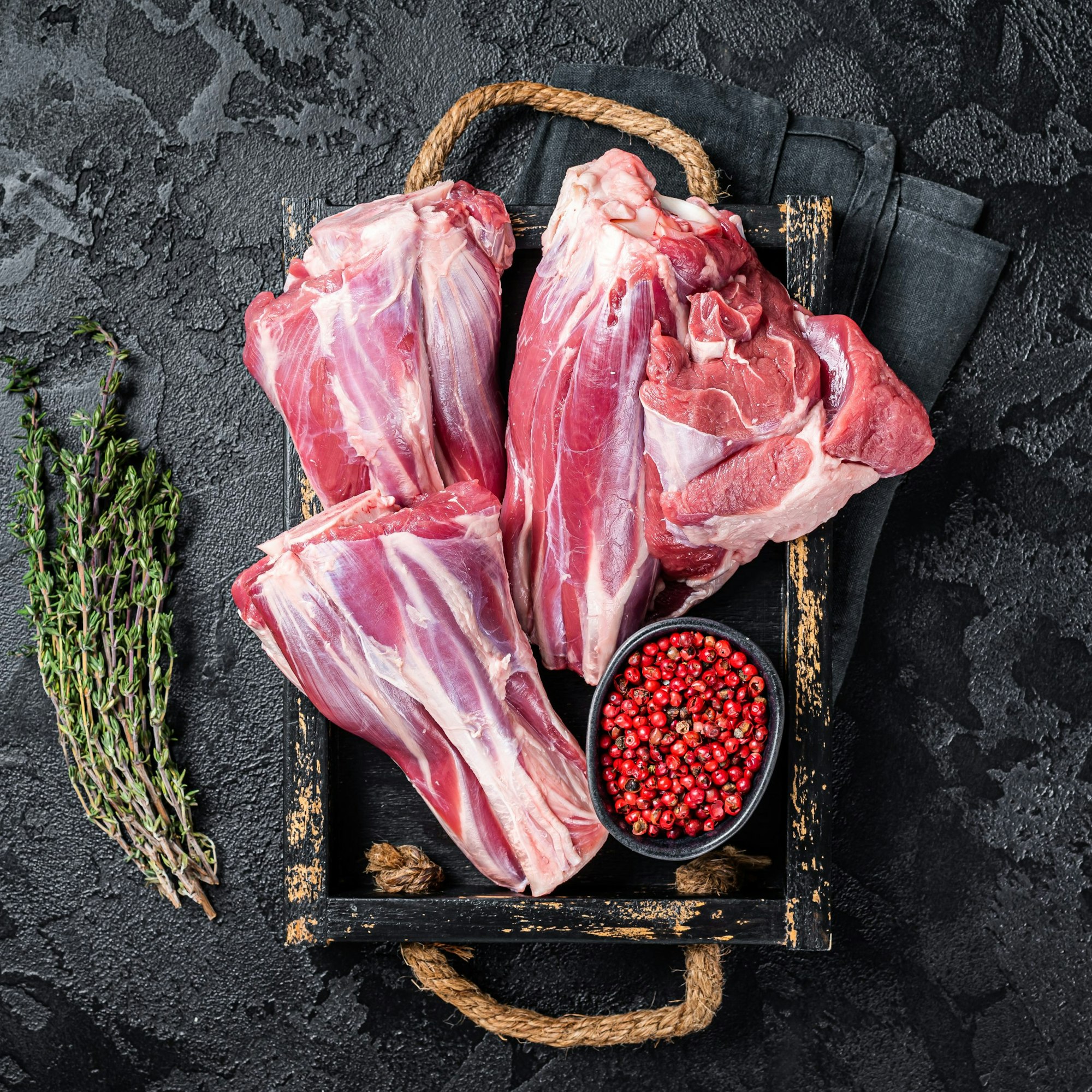 raw lamb shank on a kitchen benchtop with herbs and spices