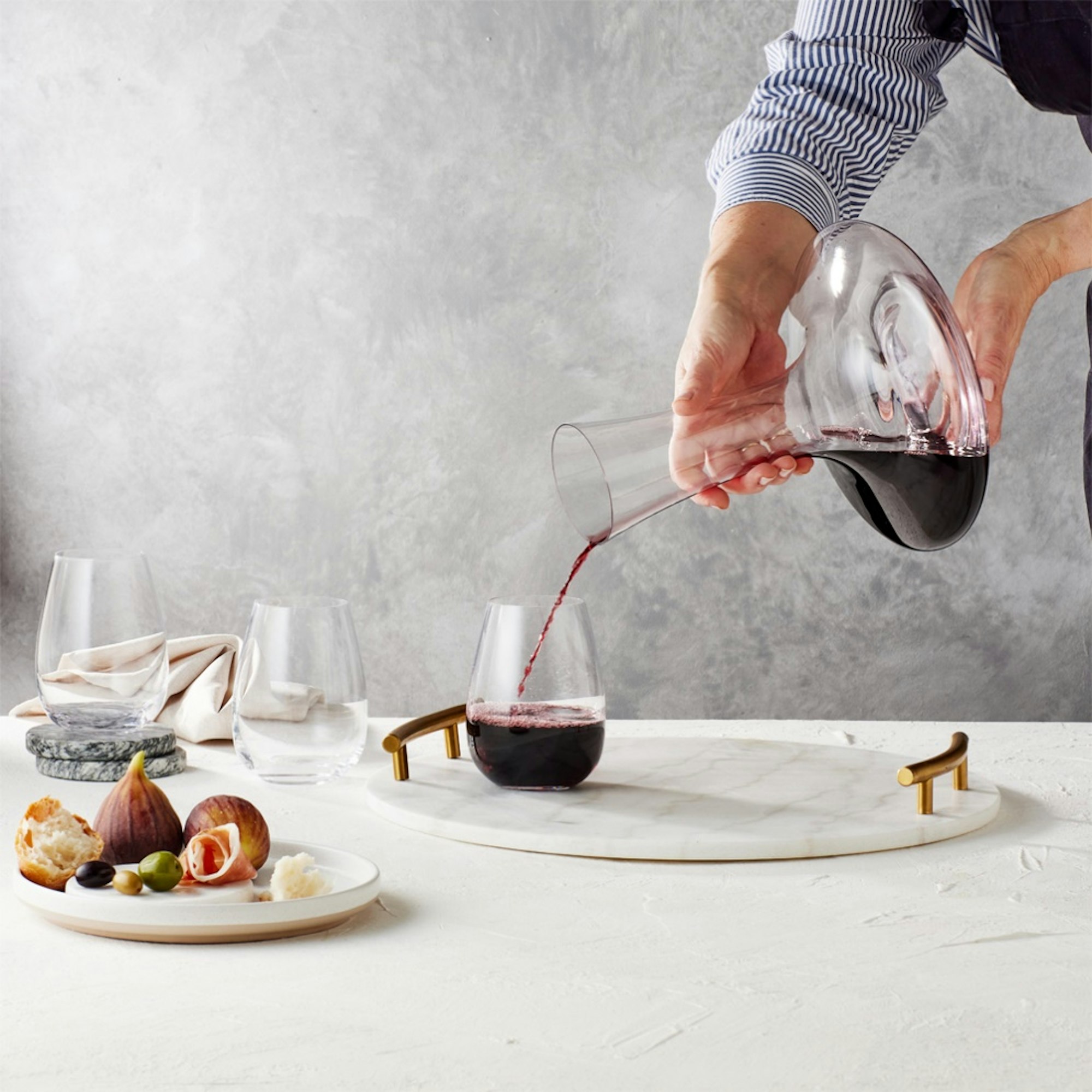 Pouring wine from decanter into wine glass served on a marble board and fruit