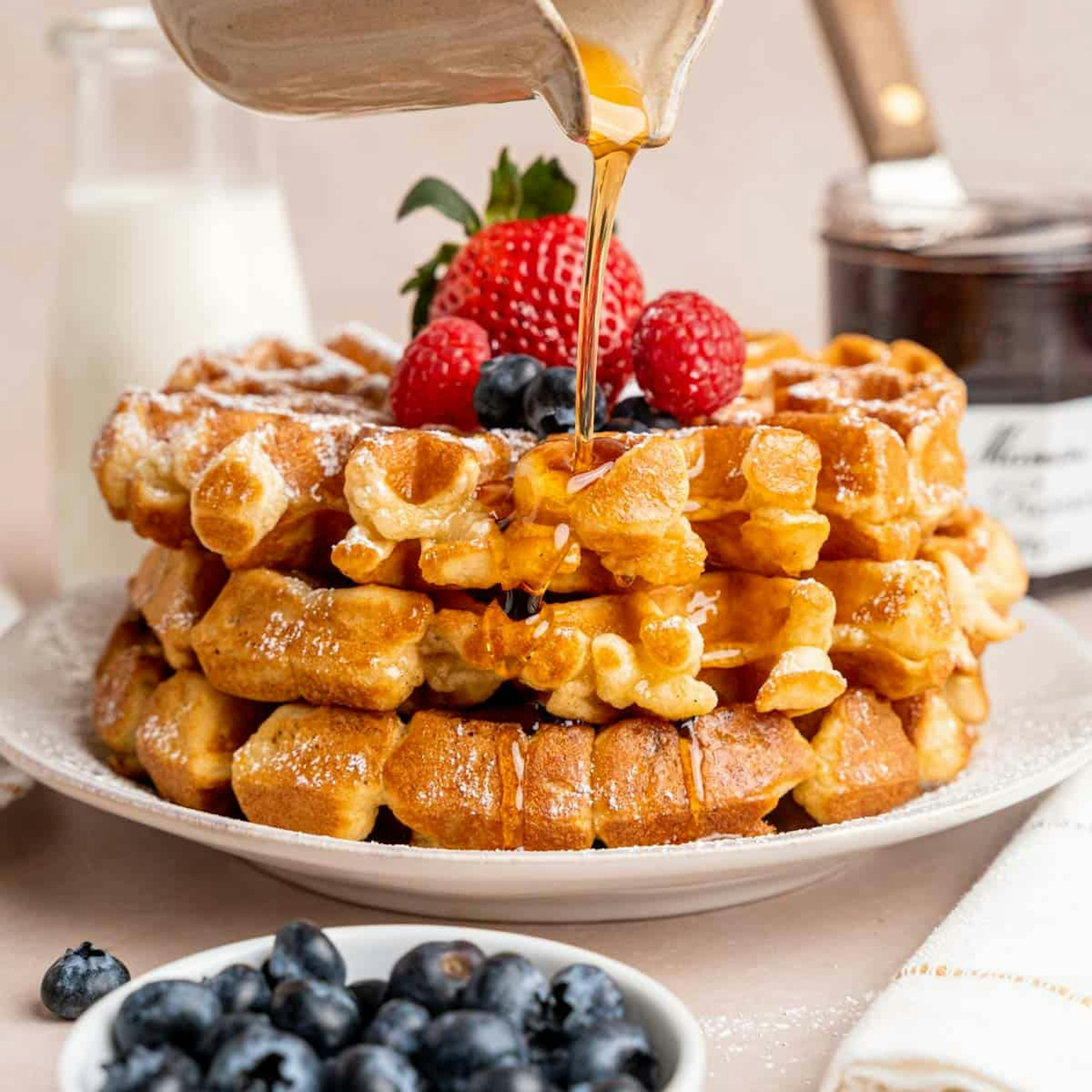 stacked belgium waffles on a plate with honey being poured over the top