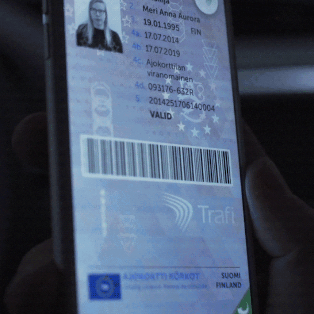 A digital driving licence shown on a smartphone screen, including a profile photo, personal details, and a barcode. The interface resembles a physical ID layout with digital security overlays.