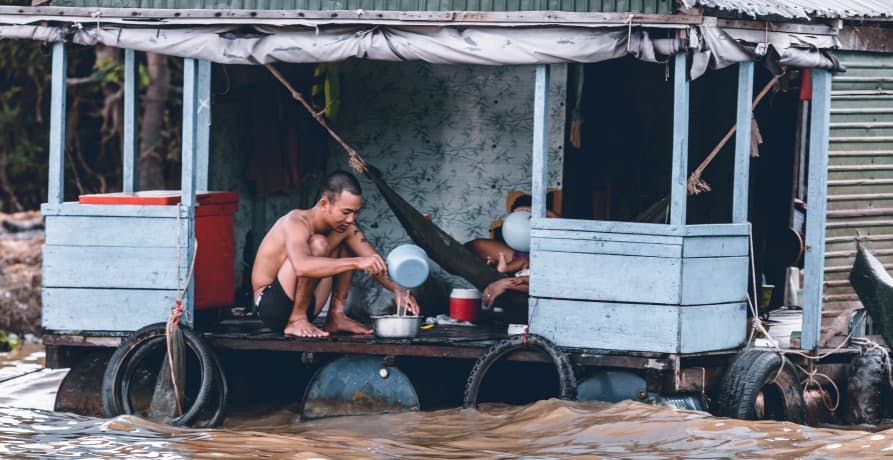 man sitting in hut above flooded river