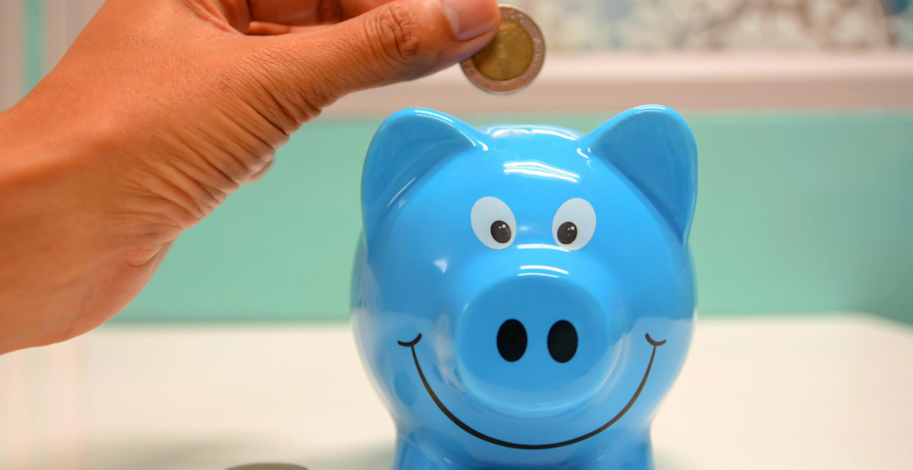 person putting coin in blue piggy bank 