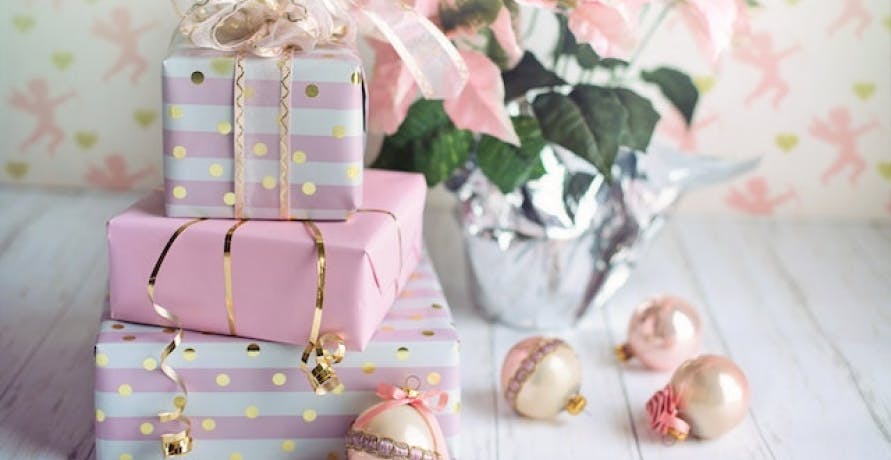pink and white presents with small plant in background and rose gold ornaments on white hardwood floor