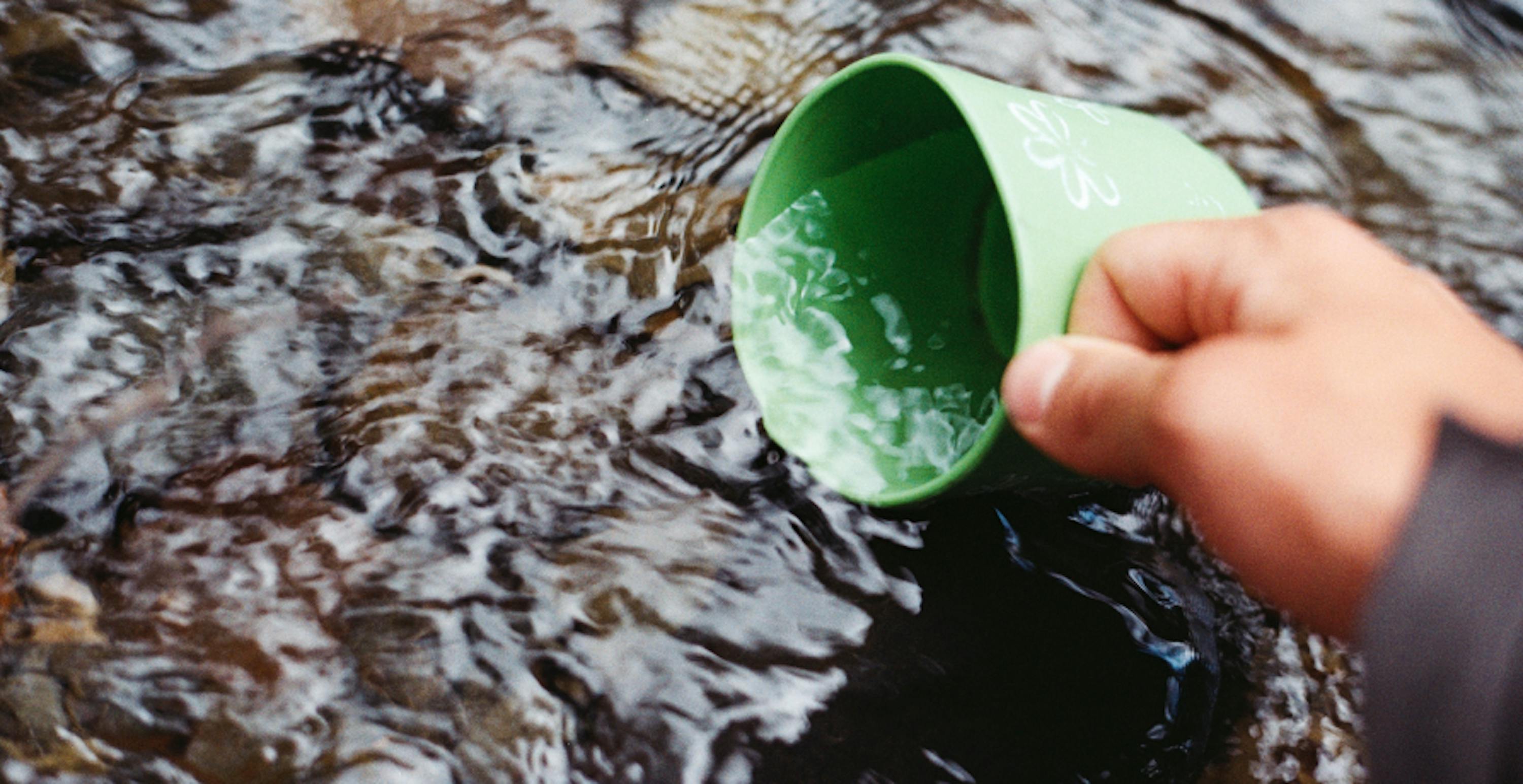 person dipping cup into river