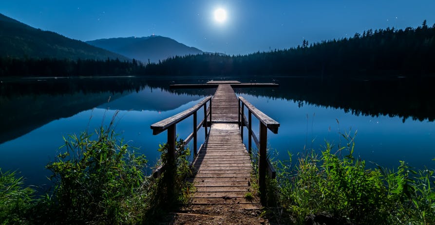 moon at dusk on lake with mountains in view