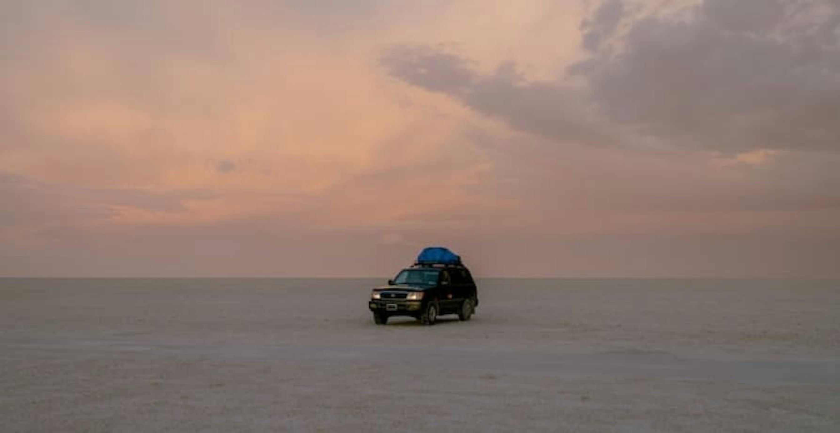car in middle of beach early sunset
