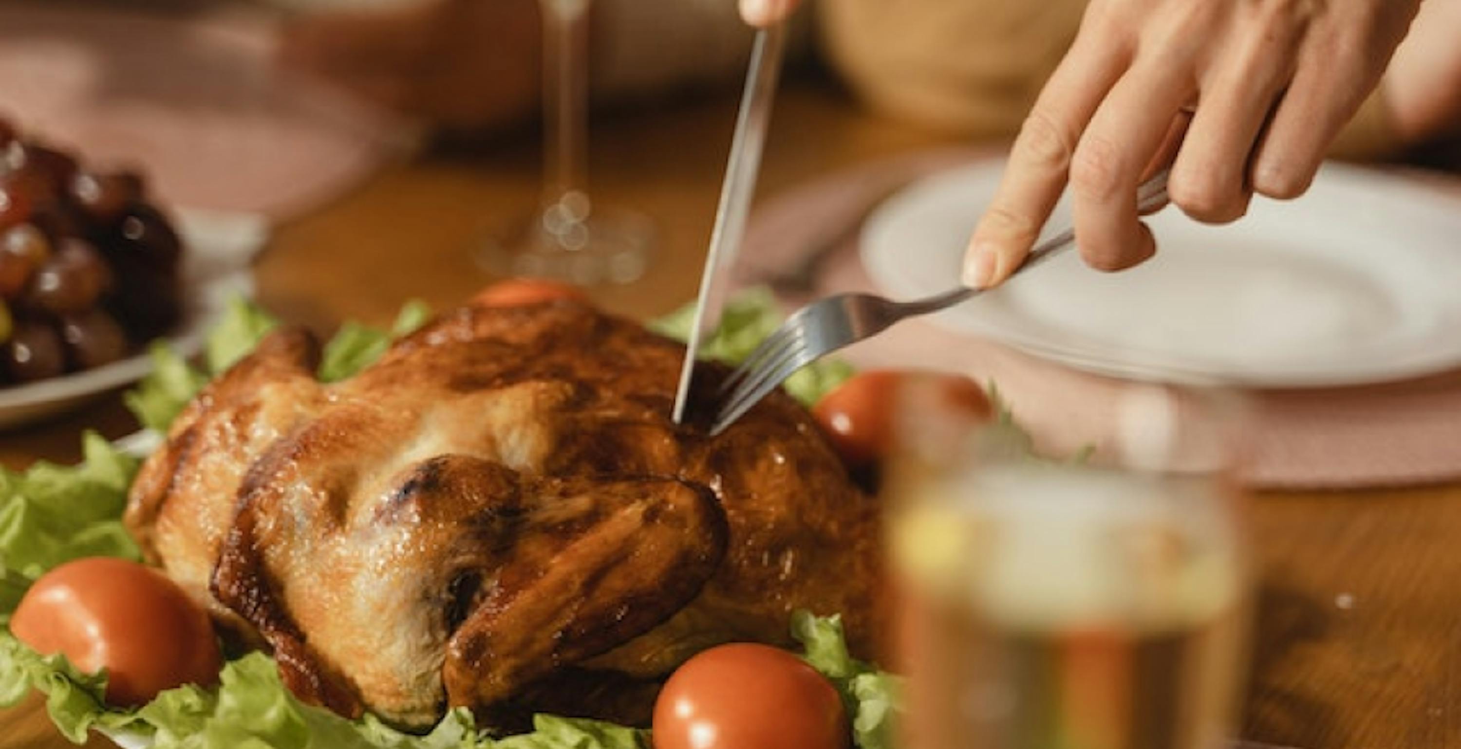 cutting small turkey on bed of greens and tomatoes on table with white plate in background