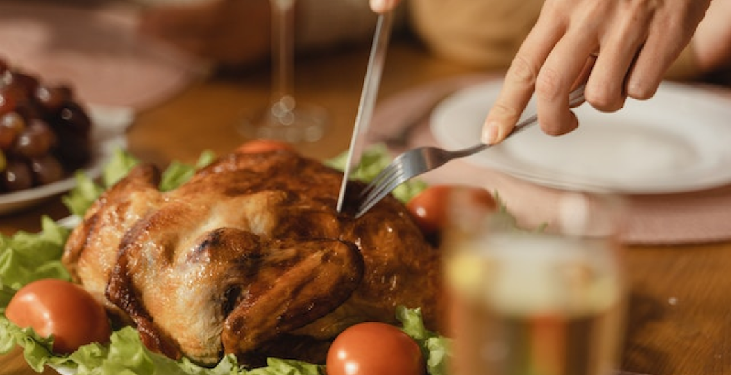 cutting small turkey on bed of greens and tomatoes on table with white plate in background