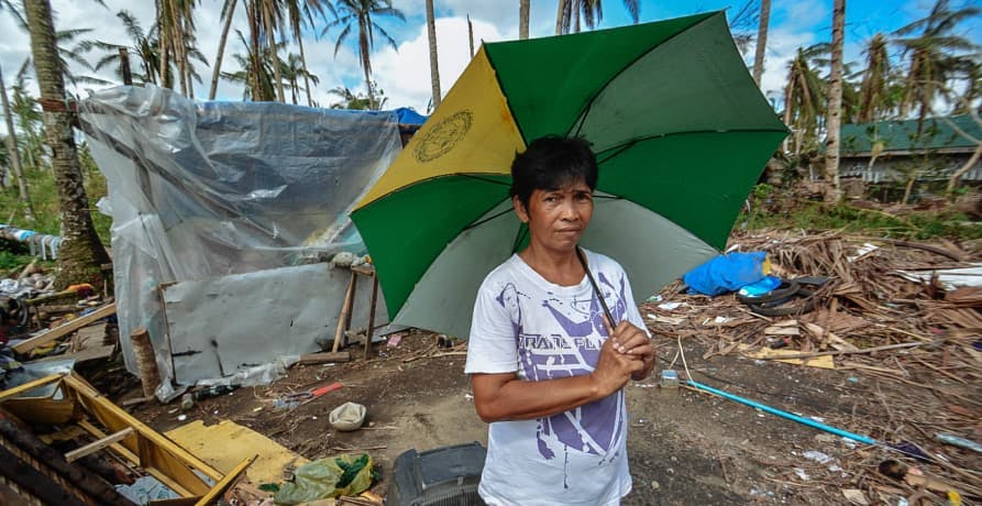 child holding up an umbrella and standing in a disaster zone