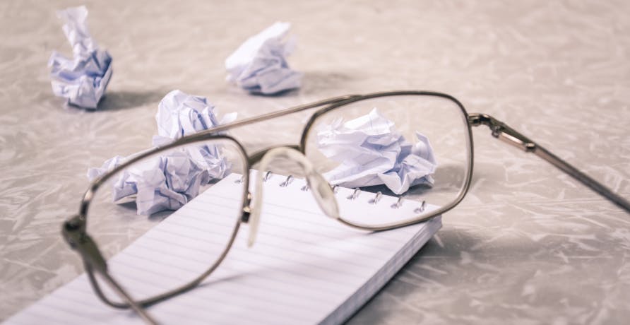 glasses on notepad with crumpled up piece of paper