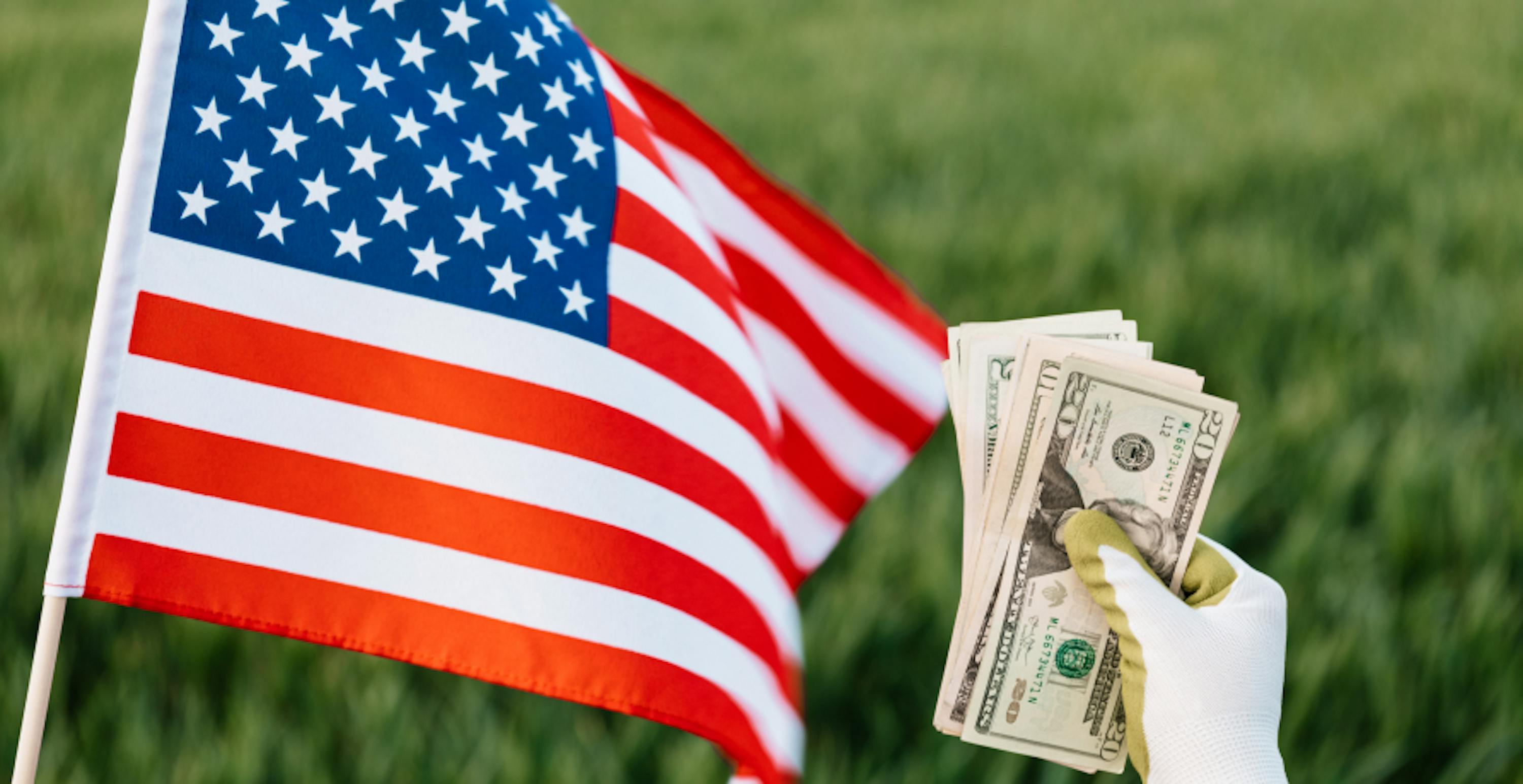 american flag and someone holding USD bills with gloves against grass