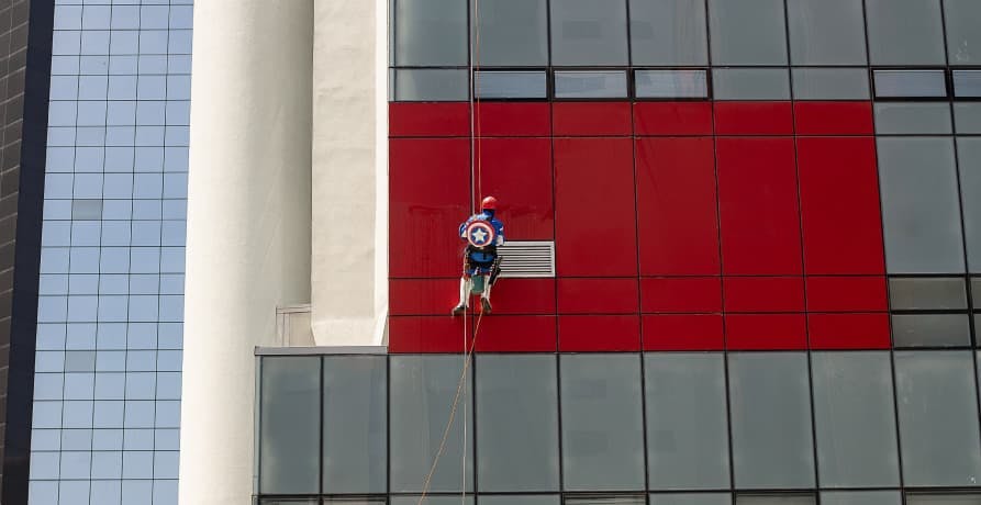 man dressed as a superhero, scaling a corporate building in protest