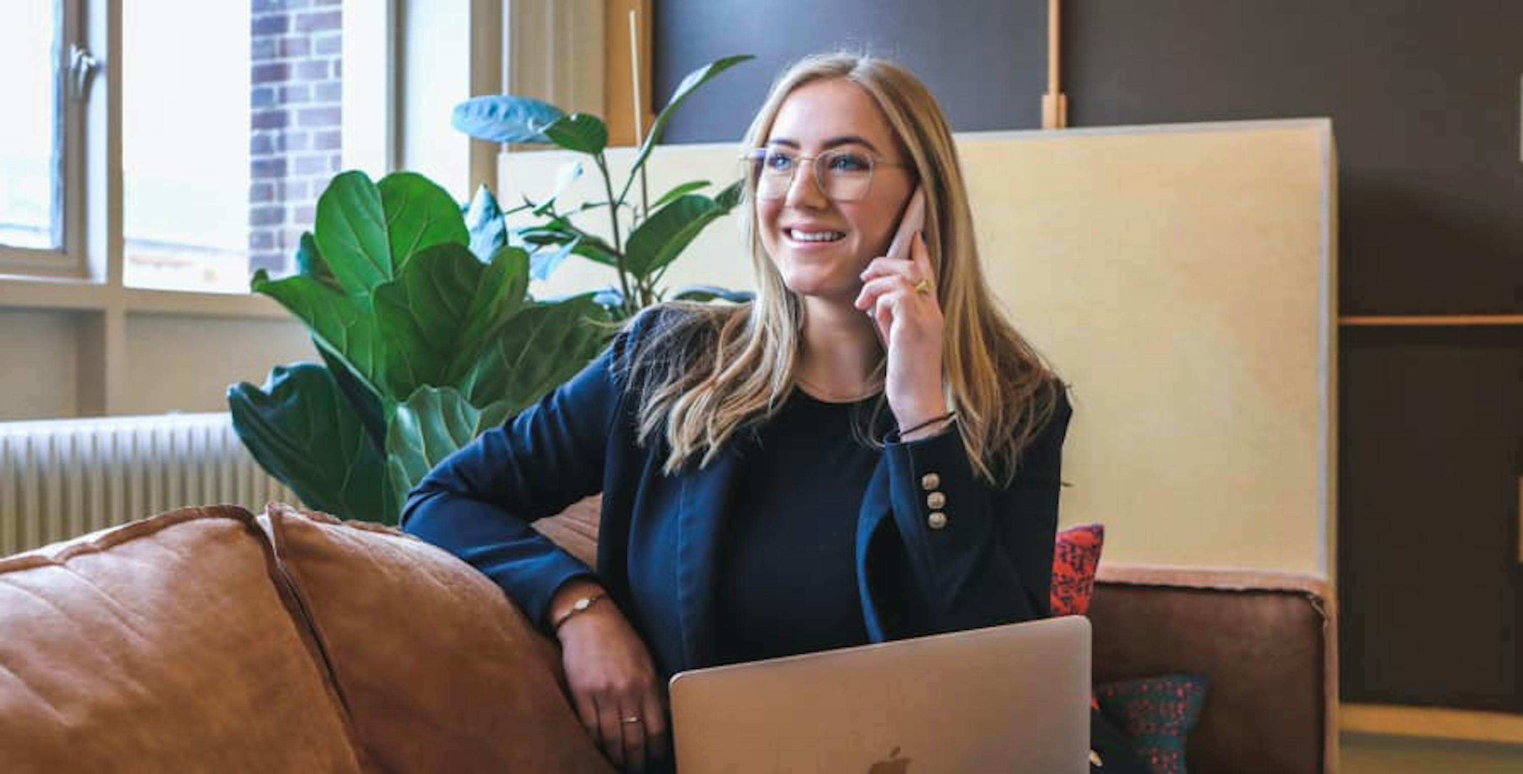 young woman blonde hair glasses on phone near plant with laptop