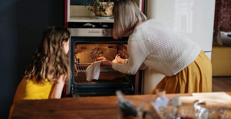 two people at the oven pulling something out