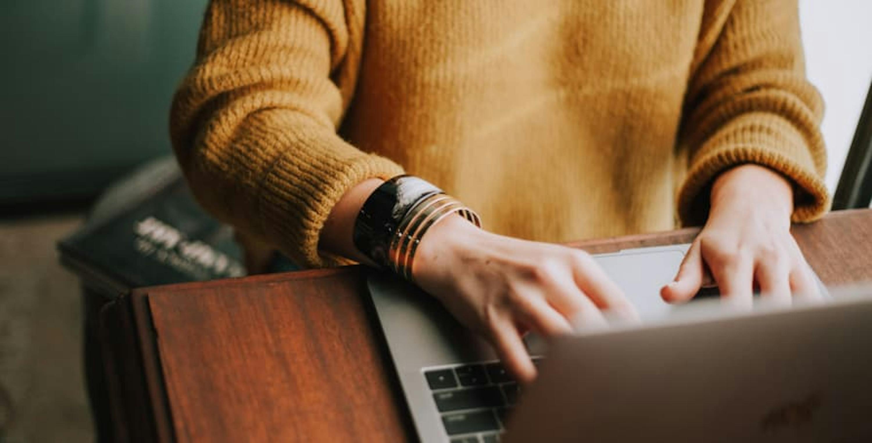 person in caramel sweater on laptop