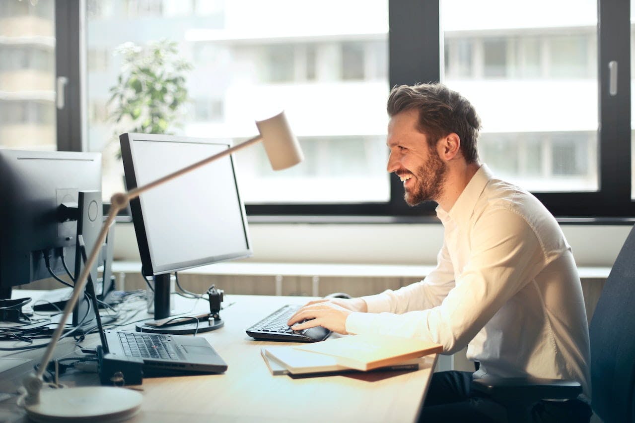 Homme en chemise blanche face à un ordinateur et souriant