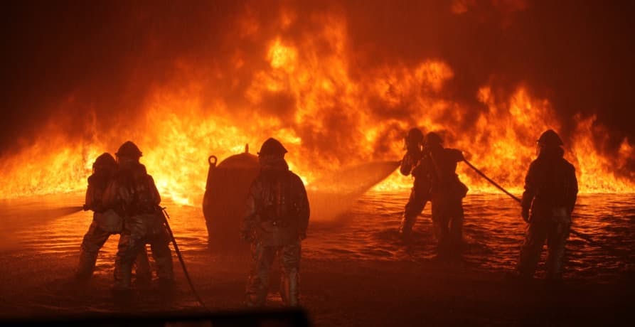 group of firefighters in front of large forest fire at night