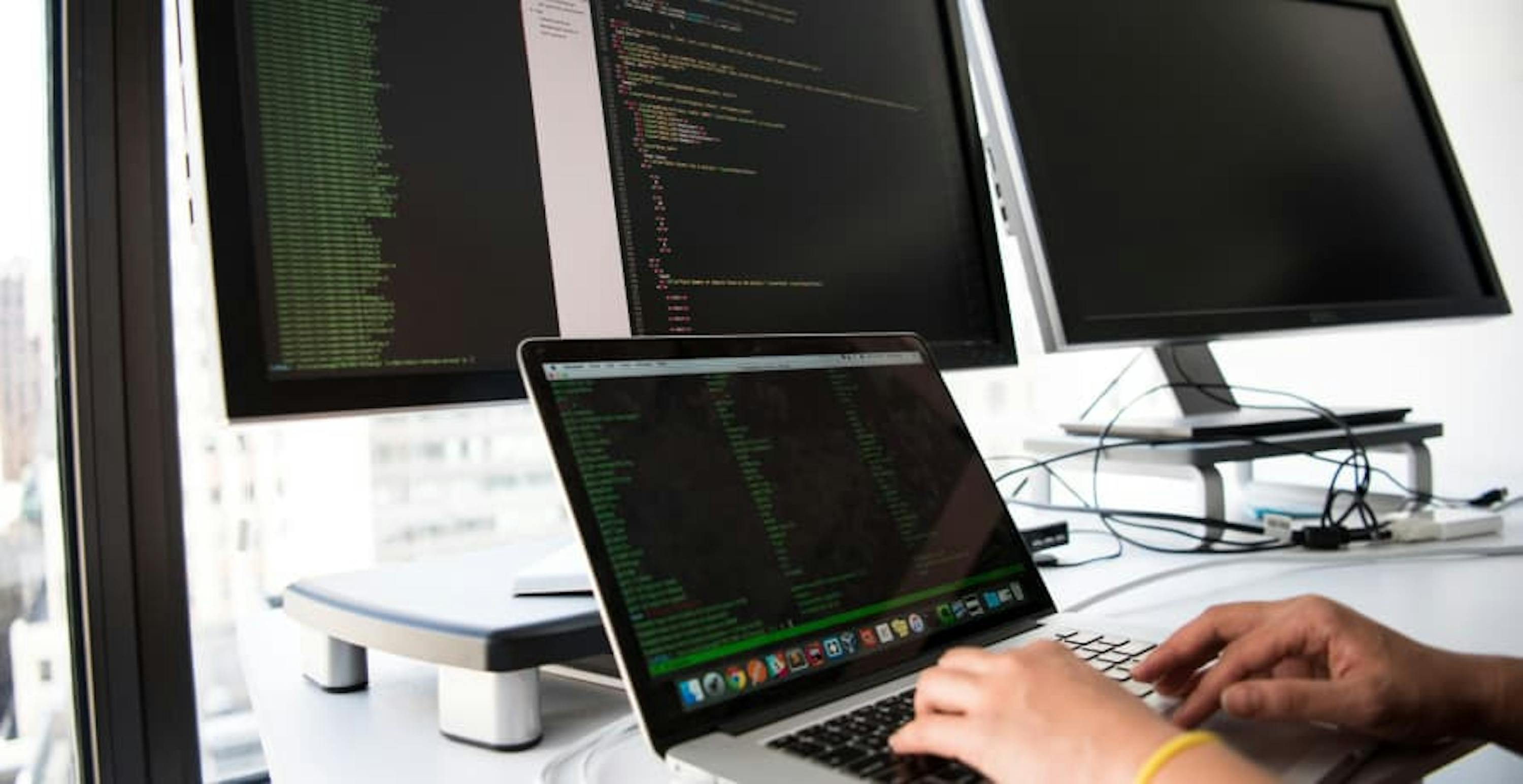 someone working on their laptop in front of multiple screens