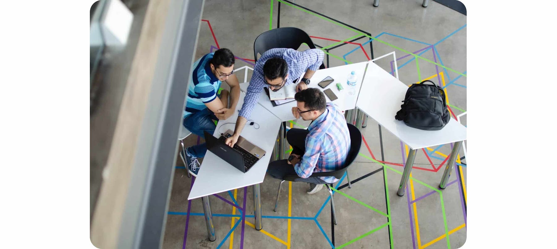 three men in a workplace looking at a laptop computer