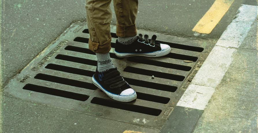 person standing over a storm drain in the street