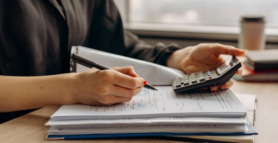 someone holding a calculator and pen, working on their accounts