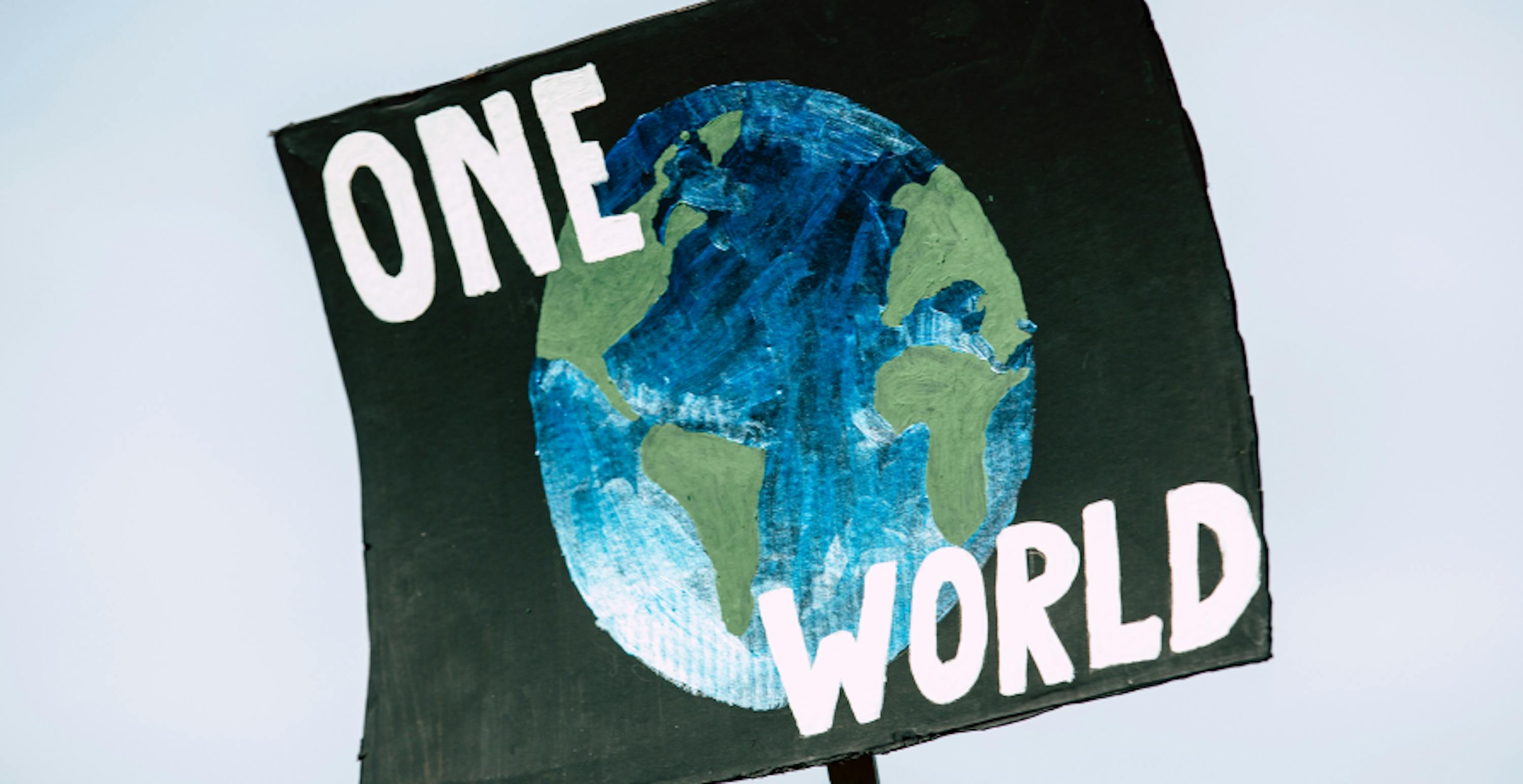 Une pancarte de manifestation d'une Terre dessinée avec l'inscription "One World"