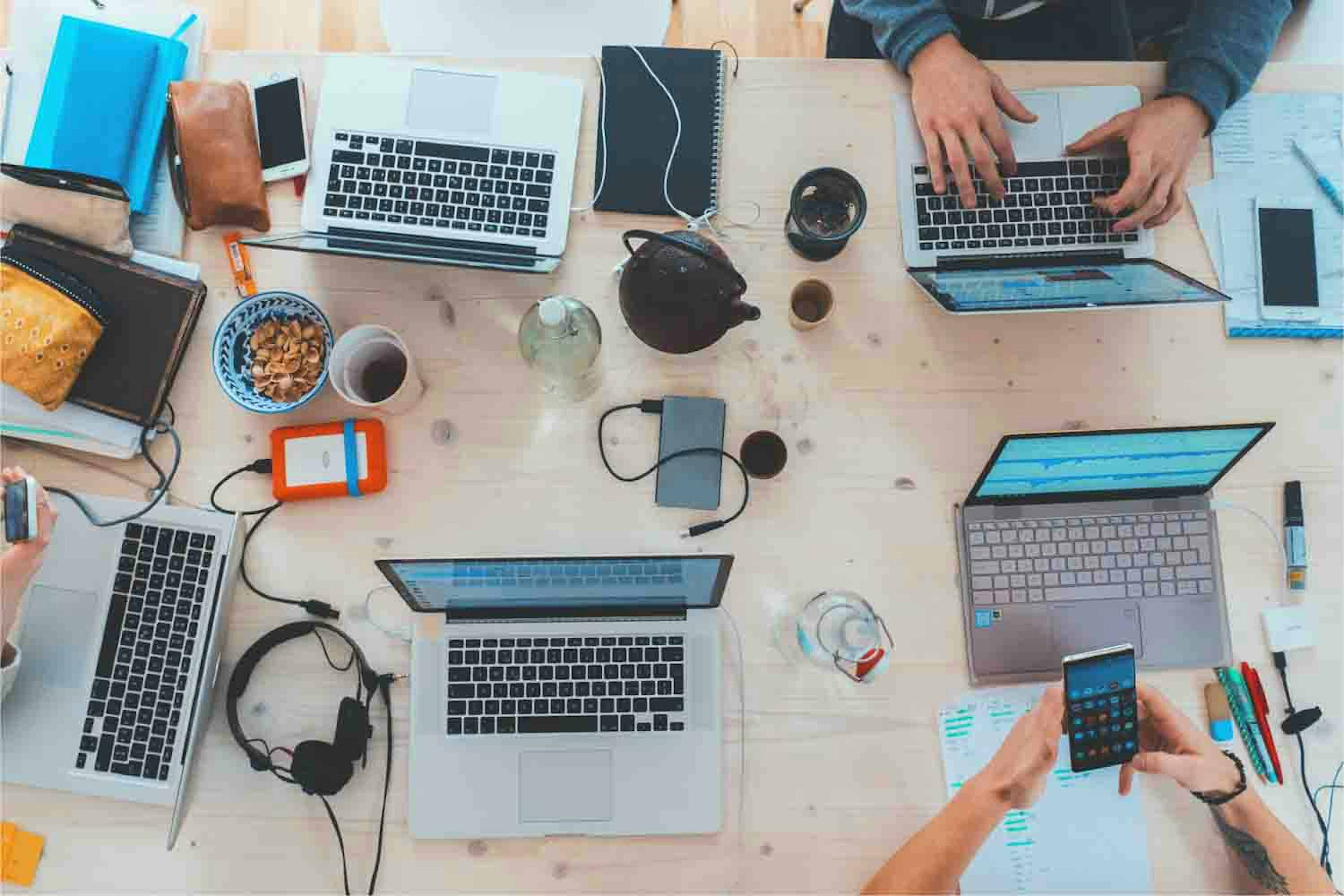 People sitting down near table with assorted laptops and phones