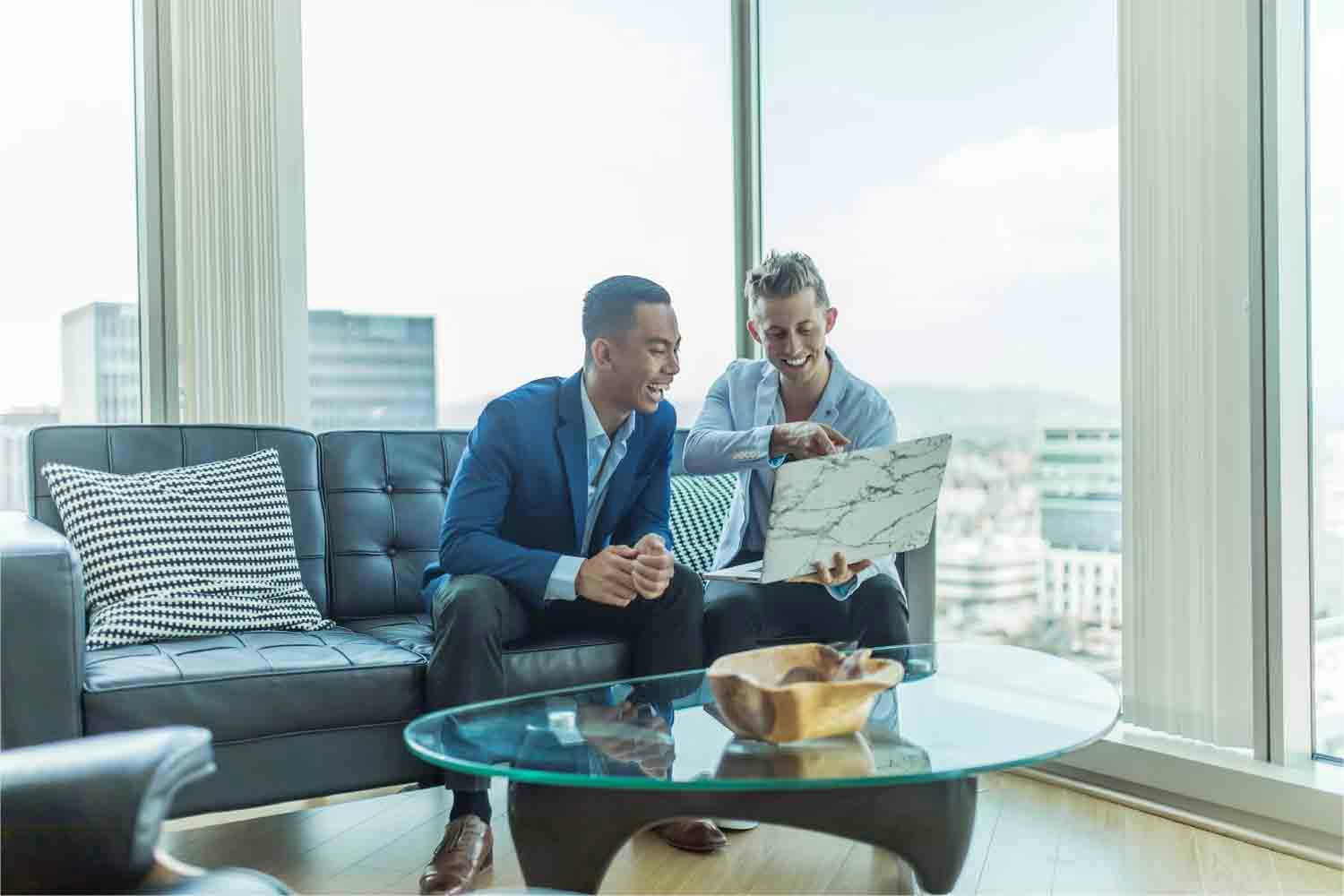 Two men in suit sitting on sofa and watching something on the laptop
