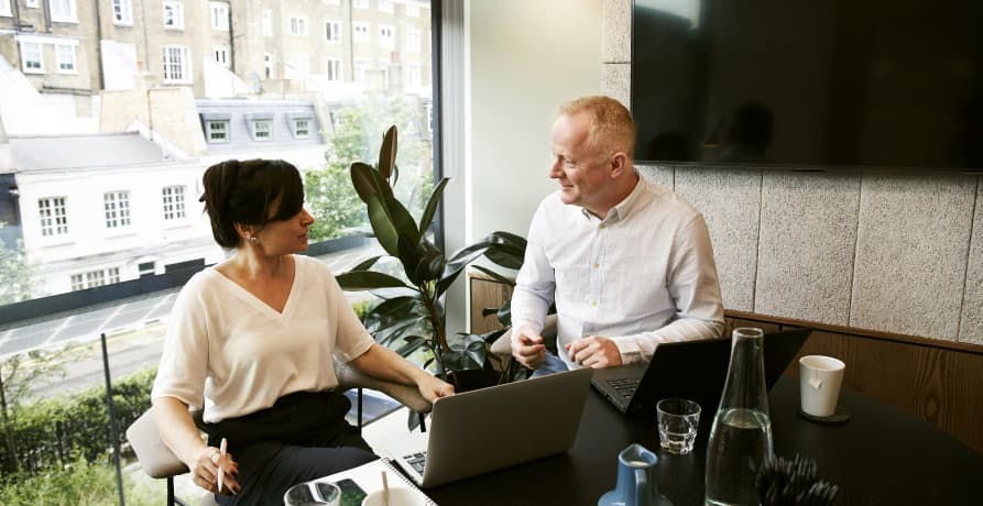 two colleagues sitting at an office desk discussing