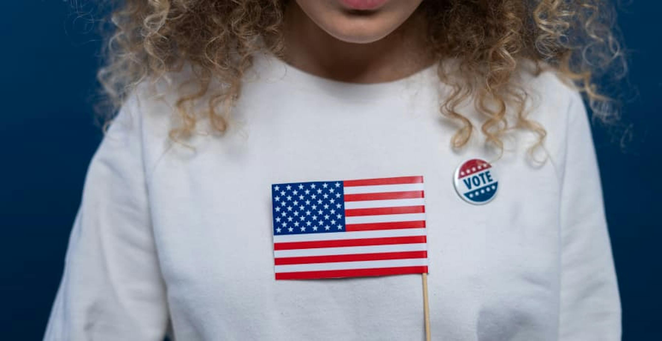 person wearin i voted pin holding american flag