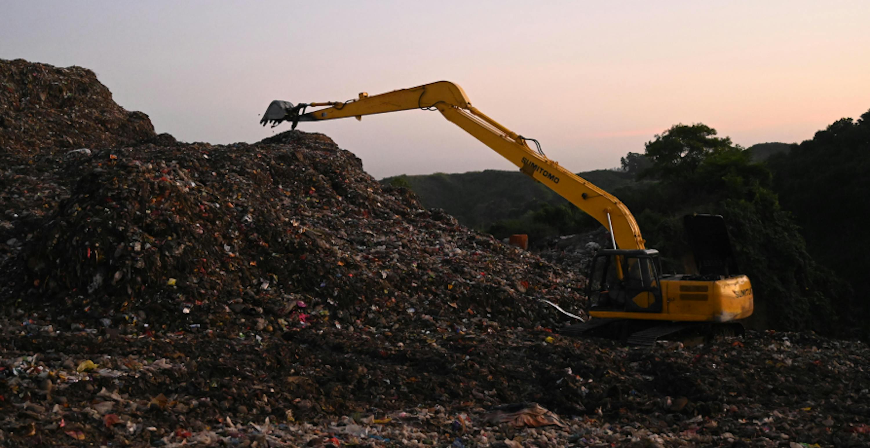 Une pelleteuse jaune en train de regrouper les déchets dans une décharge