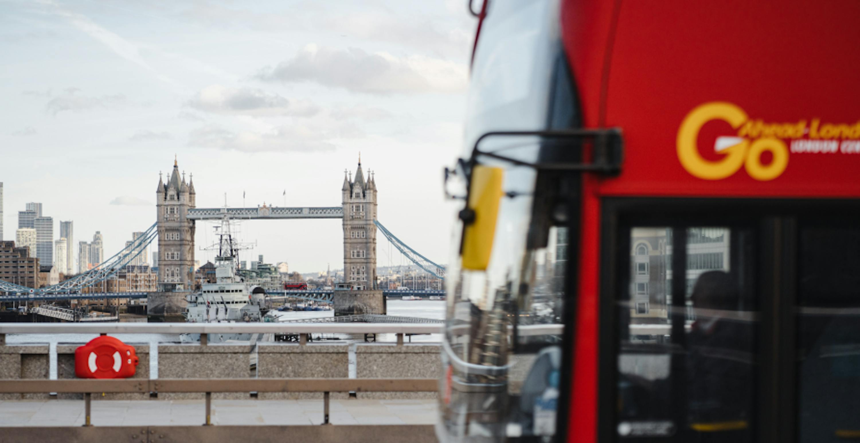 London Bus going across bridge with Tower Bridge in the distance