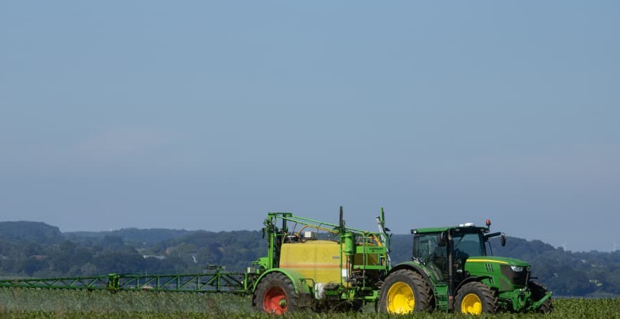 tractor in field spraying pesticides onto crops